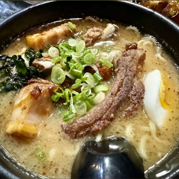 Close-up of a ramen bowl with pork belly, green onions, seaweed, and a soft-boiled egg.