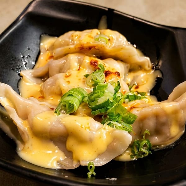 Dumplings covered in a creamy yellow sauce, chili oil, and chopped green onions in a black bowl.