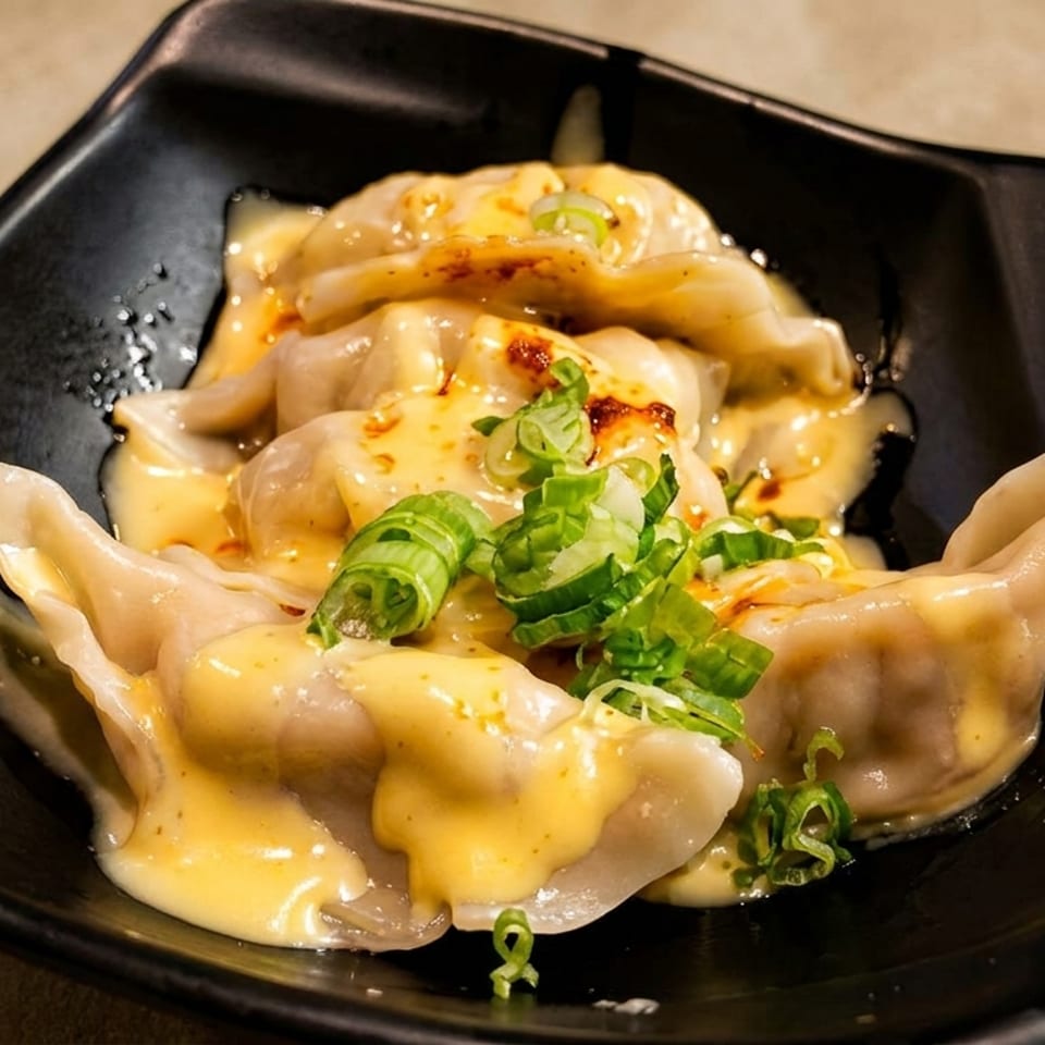 Dumplings covered in a creamy yellow sauce, chili oil, and chopped green onions in a black bowl.