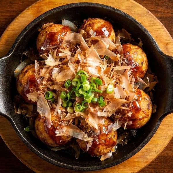 Takoyaki, Japanese octopus balls, in a black cast iron pan, topped with bonito flakes and green onions.